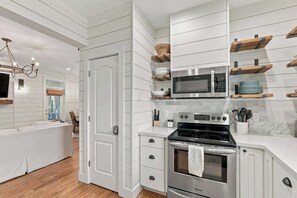 A modern kitchen with white cabinetry, a stainless steel stove, and a microwave. - Beach cottage w/ heated pool & fenced yard (Panama City Beach)