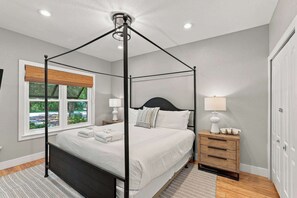 Una cama con dosel sobre una base de madera, ropa de cama blanca y una mesita de noche con una lámpara.
