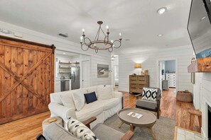 A spacious living room with a large wooden door, a white sofa, a coffee table, and a chandelier. - Beach cottage w/ heated pool & fenced yard (Panama City Beach)