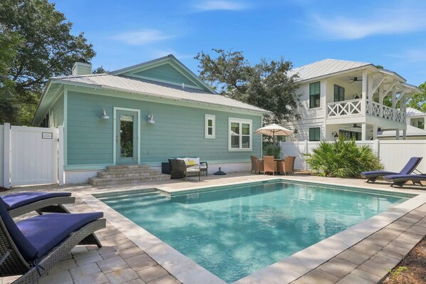 A residential property with a swimming pool, a covered patio, and a white fence.