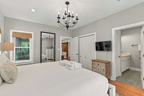A bedroom with a large bed, a chandelier, a dresser, a television, and a bathroom with a sink and toilet.