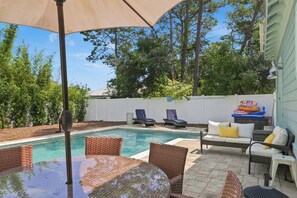 Un patio trasero con piscina, sillas de descanso, una mesa y un área de patio techada.