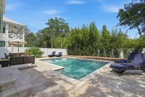 A rectangular swimming pool with a white border, surrounded by a paved patio area.