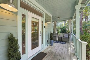 Een overdekt terras met houten vloer, een zithoek met twee stoelen en een bloempot.