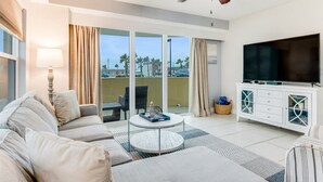 A modern living room with a sofa, a coffee table, a TV, and a balcony with curtains.