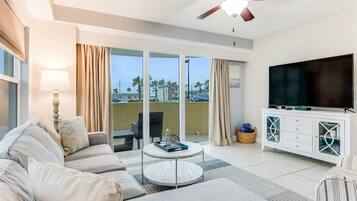 Moderni olohuone, jossa on sohva, sohvapöytä, televisio ja parveke, jossa on verhot.