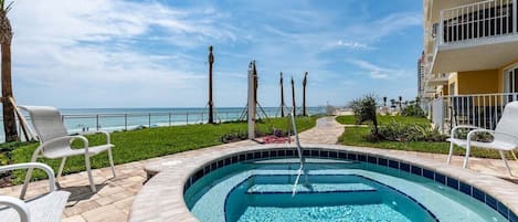 A swimming pool with lounge chairs, a clear view of the ocean, and a building with balconies.