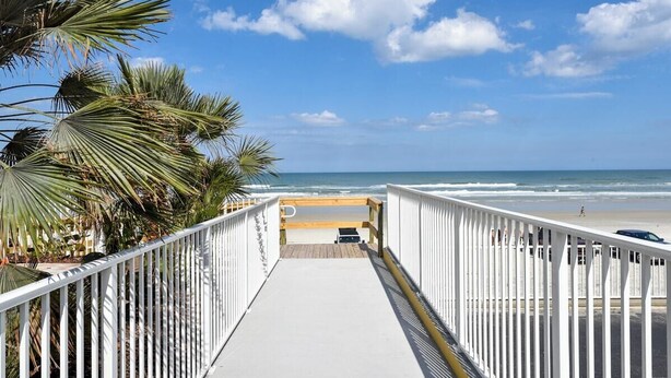 A wooden deck leading to a beach with palm trees on the left.