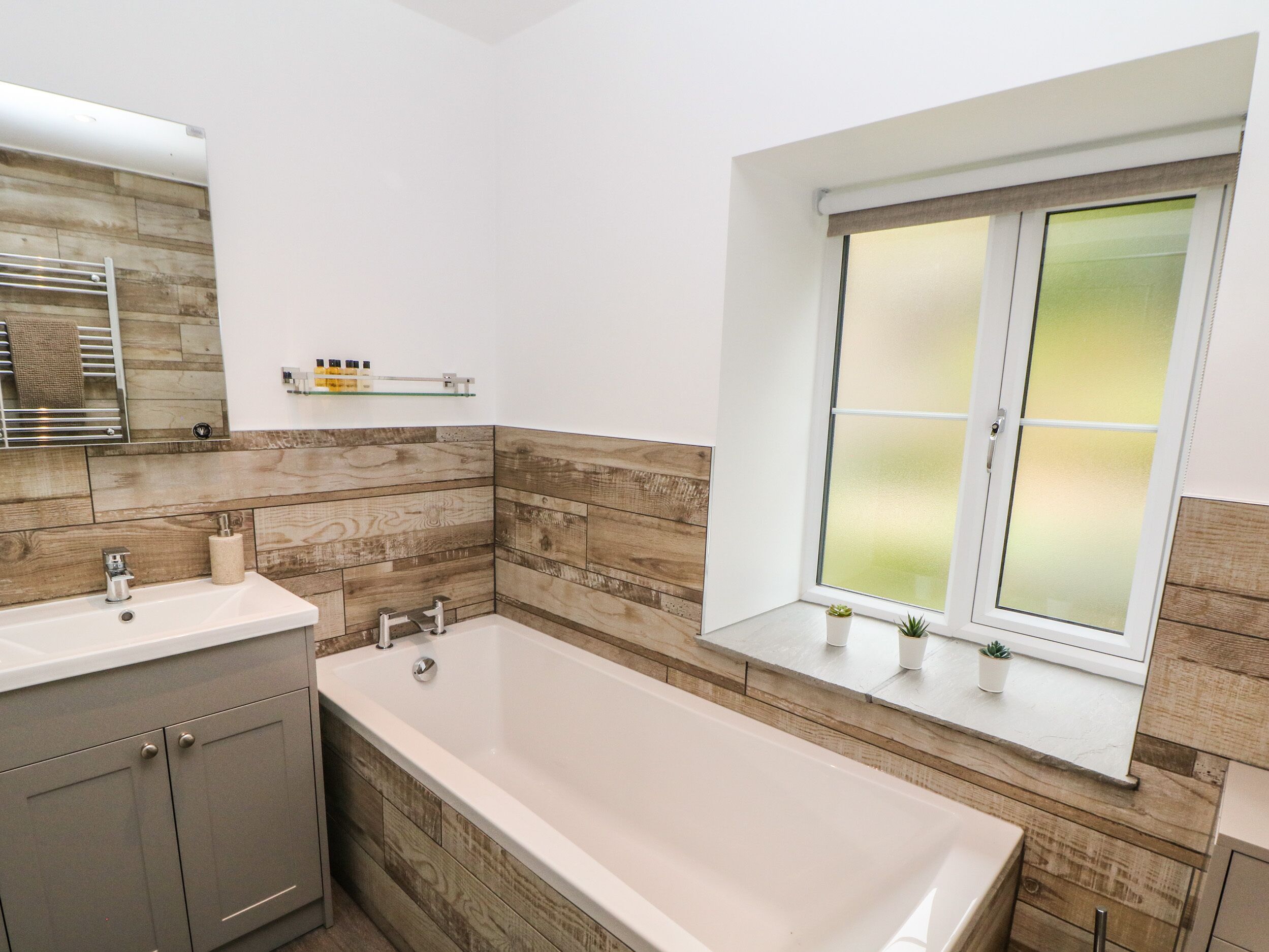 Un baño moderno con una bañera independiente, un tocador con espejo y una ventana con cristal satinado.