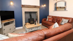 Una sala de estar con un sofá de cuero marrón, un televisor de pantalla plana sobre un mueble de madera, una chimenea y una pared de piedra.