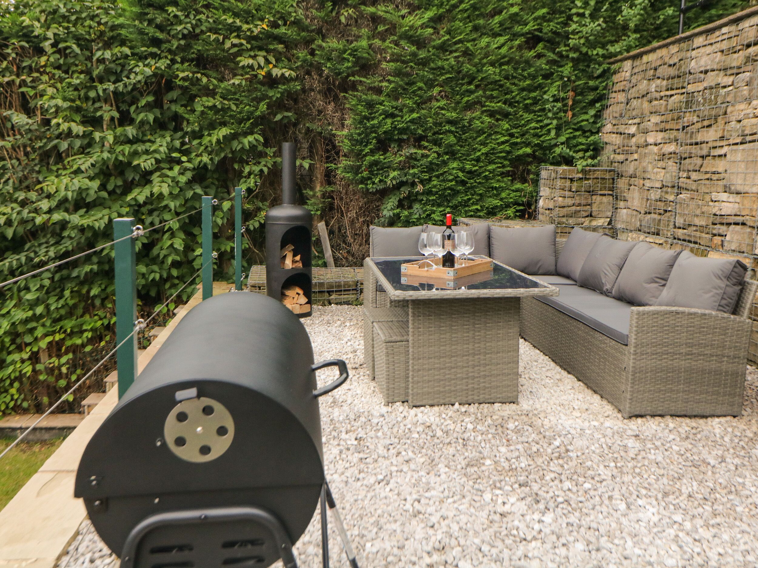 An outdoor patio with a grill, wicker furniture, and a stone wall.