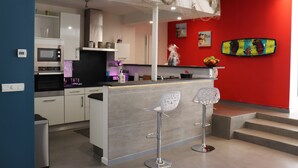 A modern kitchen with white cabinets, a central island with bar stools, and a red accent wall.
