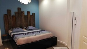 A bedroom with a bed, a wooden headboard, a blue wall, a white door, and a small rug.