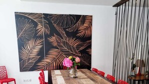 A dining area with a wooden table, red chairs, and a large wall art piece.