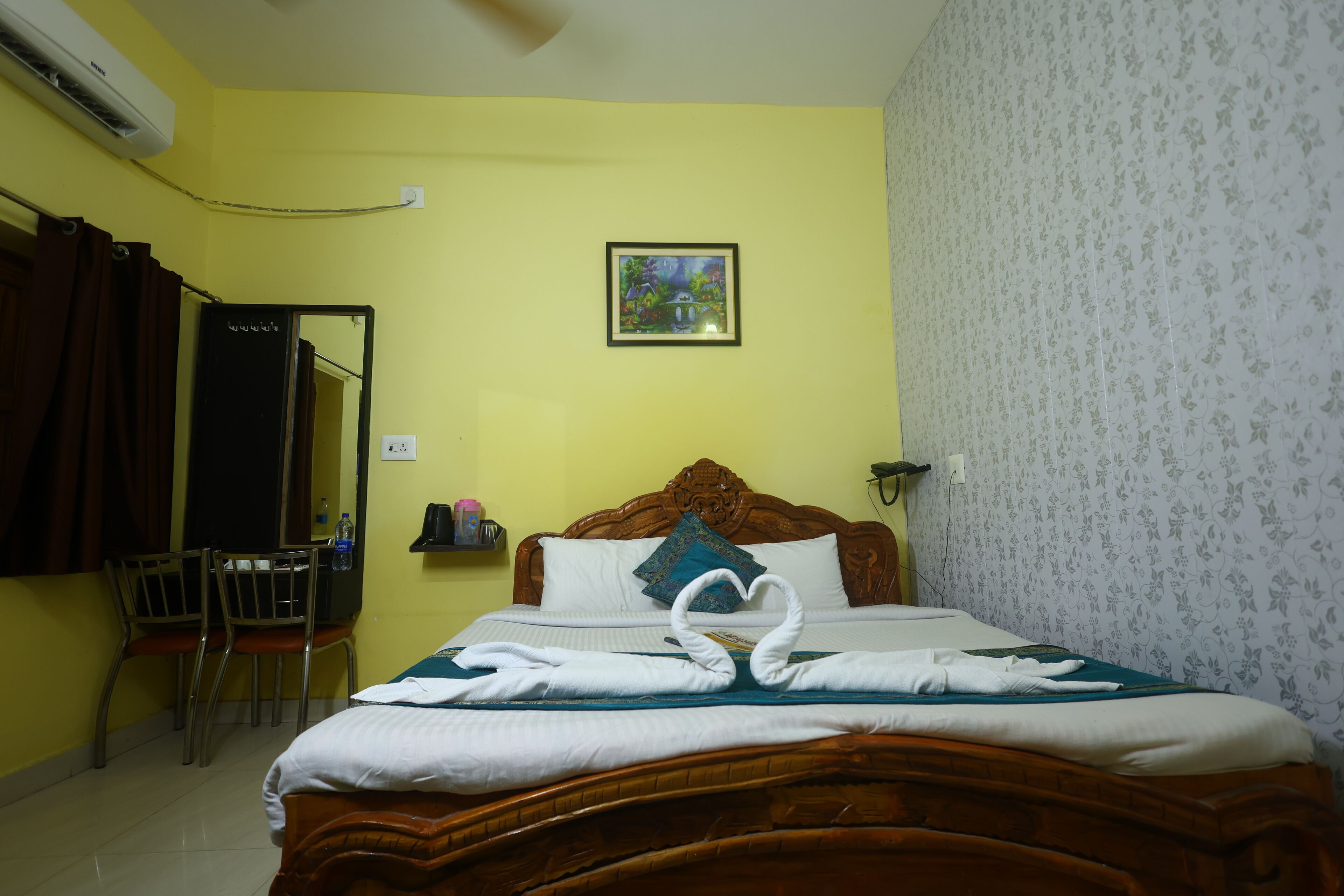 A hotel room with a wooden bed, a mirror, a picture on the wall, and a desk with chairs.