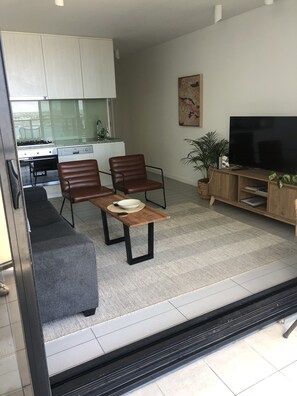 A modern living room with a sofa, two chairs, a coffee table, a TV, and a kitchen in the background.