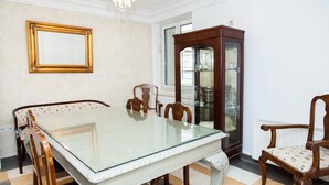 A dining room with a glass-top table, wooden chairs, a cabinet, and a window with blinds. - Chic Charming Central Athens Apt. (Athens)