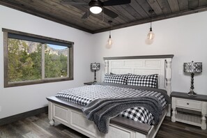 Relax in this serene bedroom with a large bed, white headboard, and checkered bedspread, offering a peaceful view of the surrounding trees and mountains.