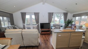 A spacious living area with a sofa set, a television, and a kitchen area with a counter and cabinets. - Hillside View (Morpeth)