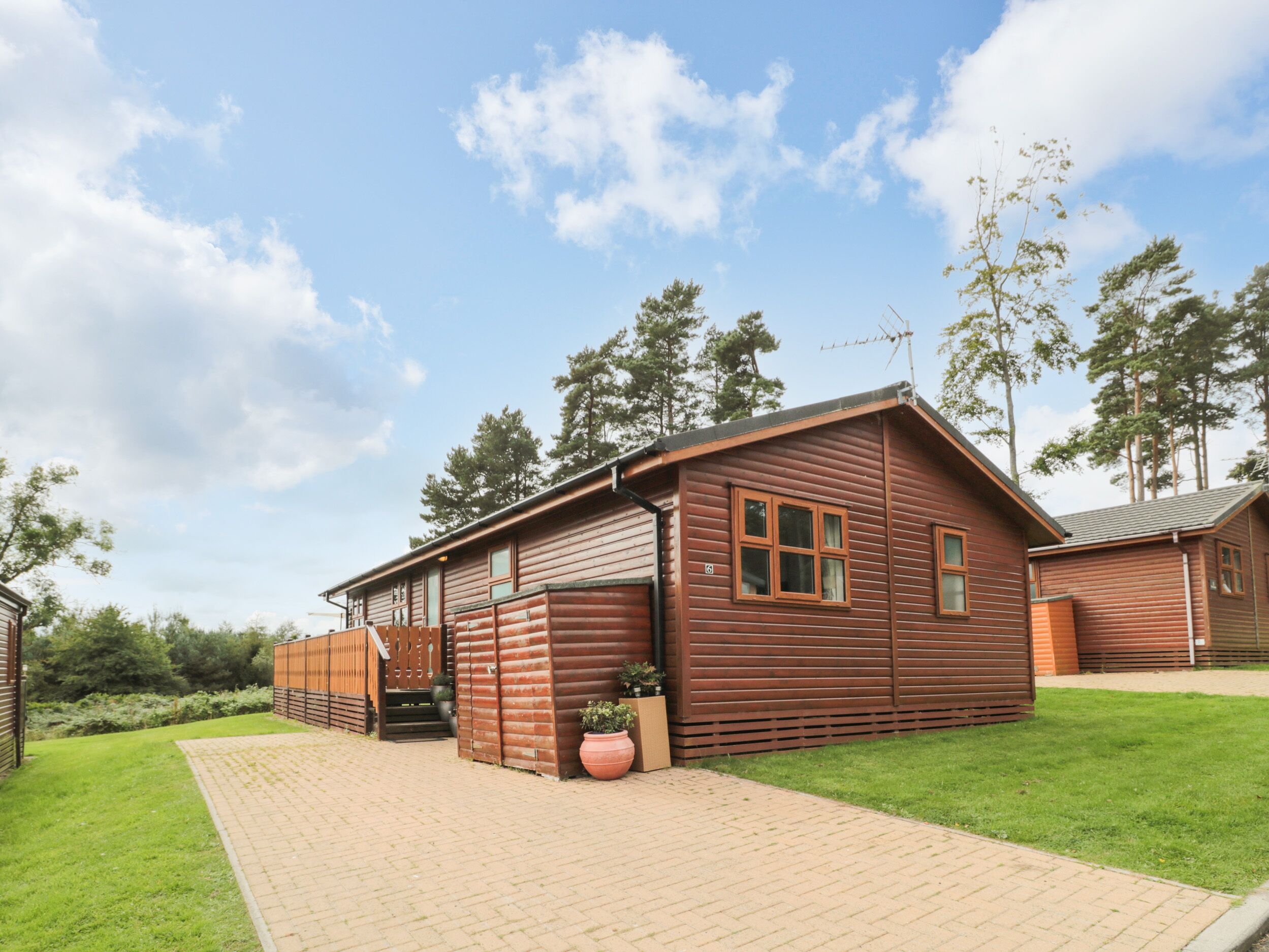 A wooden cabin with a brick pathway leading to the entrance, surrounded by greenery and trees.