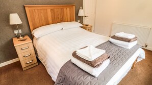 A neatly made double bed with a wooden headboard, a bedside table with a lamp, and a radiator on the wall. - Hillside View (Morpeth)