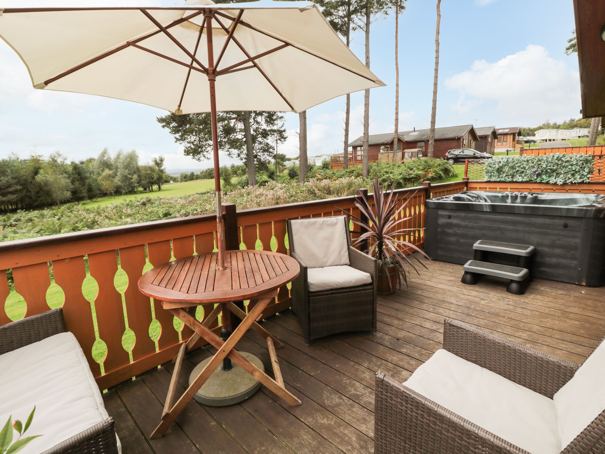 A wooden deck with outdoor furniture, including a table and chairs, a large umbrella, and a hot tub.
