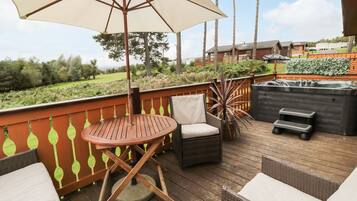 A wooden deck with outdoor furniture, including a table and chairs, a large umbrella, and a hot tub.