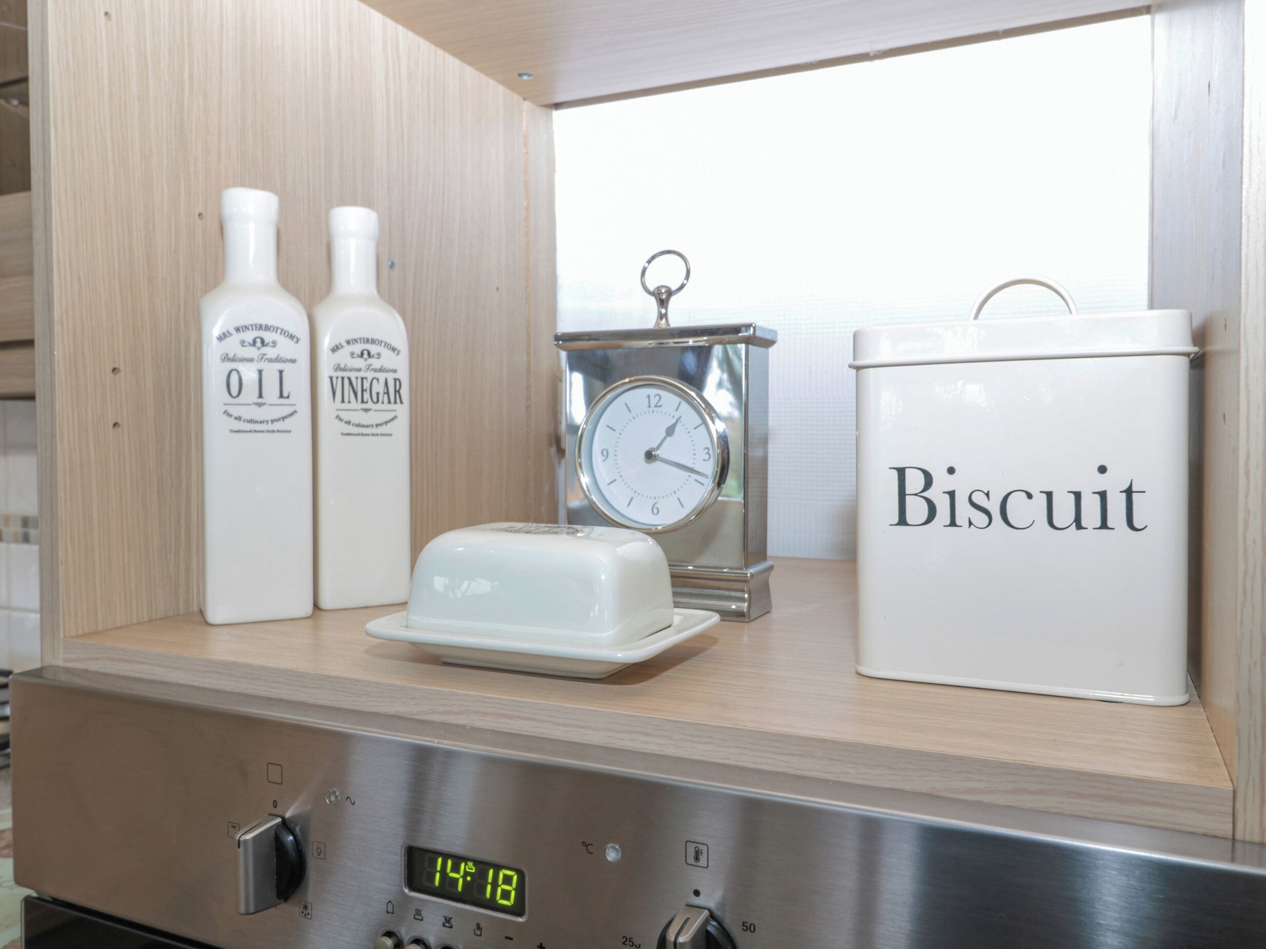 Un comptoir de cuisine avec des bouteilles étiquetées « HUILE » et « VINAIGRE », une horloge et un récipient étiqueté « BISCUIT ».