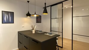 A modern kitchen with a central island, pendant lights, and a glass partition wall.