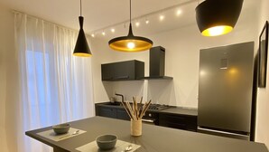A modern kitchen with a central island, pendant lights, and a stainless steel refrigerator.