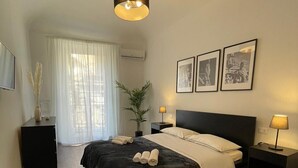 A bedroom with a bed, bedside tables, a hanging light fixture, a window with curtains, and framed pictures on the wall.