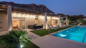 A modern poolside area with a pool, lounge chairs, and a covered seating area. - Villa Samiram (Ierapetra)