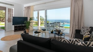 A modern living room with a large TV, comfortable seating, a dining area, and a view of the ocean. - Villa Samiram (Ierapetra)