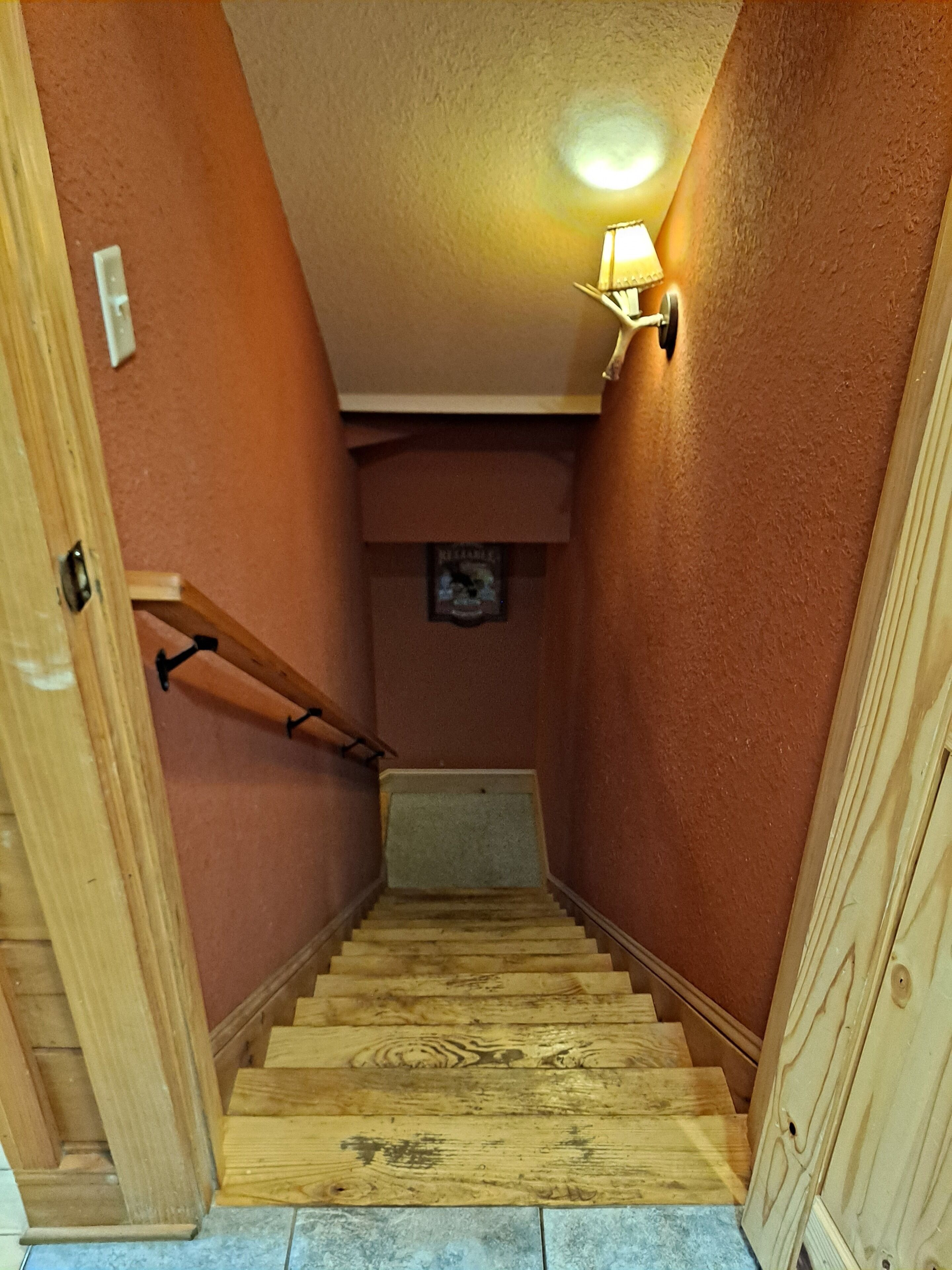 A wooden staircase with a handrail, a wall-mounted light fixture, and a small plaque on the wall.