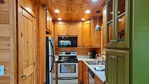 A compact kitchen with wooden cabinets, a refrigerator, an oven, and a sink.