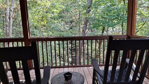 A wooden deck with two chairs and a small table, overlooking a forested area.
