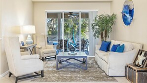 A living room with a sofa, armchairs, a coffee table, and a large window with a view of palm trees.