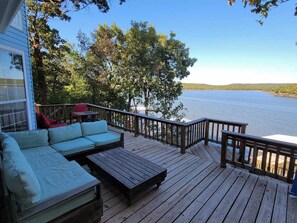 Une terrasse en bois avec un canapé et une table, donnant sur une étendue d’eau et entourée d’arbres.