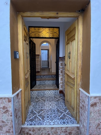 A narrow hallway with patterned tile flooring, wooden doors, and a tiled wall.