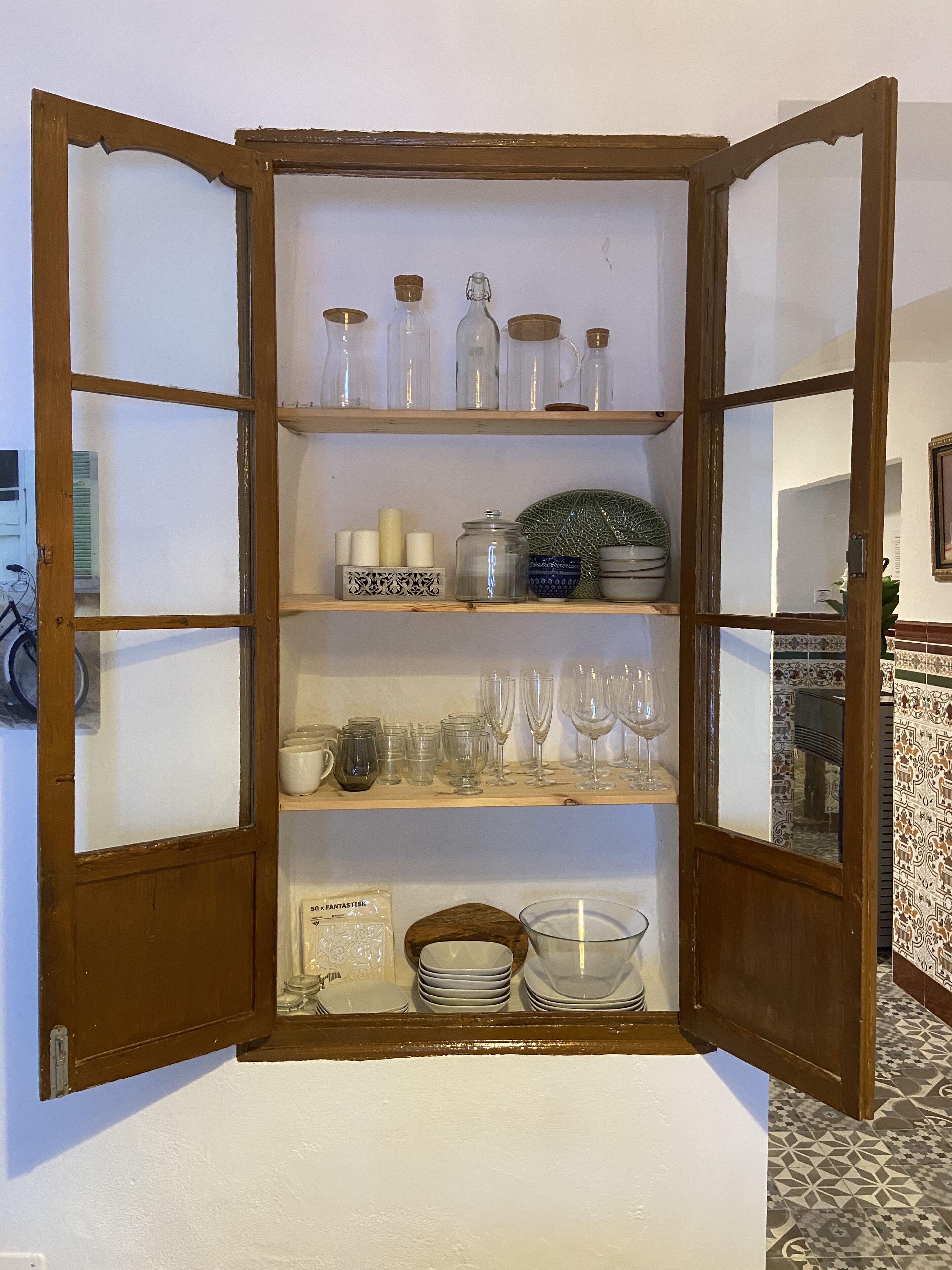 Un mueble de madera con varios estantes que contiene cristalería, velas y objetos decorativos.