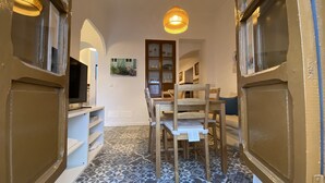 A narrow hallway with patterned floor tiles, a wooden chair, a television on a white shelf, and a wooden cabinet with glass doors. - Traveler's House (Setenil de las Bodegas)