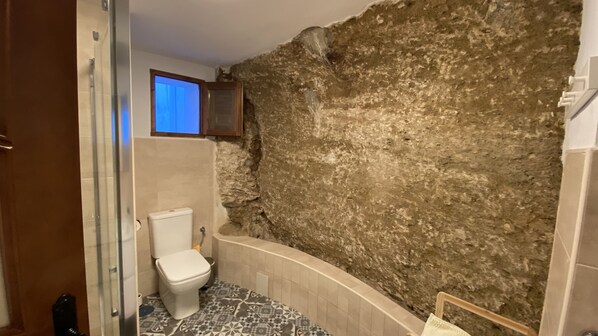 Une salle de bain avec un mur en pierre, des toilettes et des carreaux de sol à motifs.