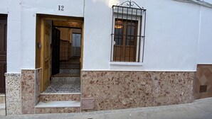 A building with a number 12 sign, a window with a metal grille, and a door leading to a tiled interior. - Traveler's House (Setenil de las Bodegas)