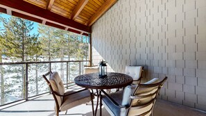 Un espace extérieur abrité, aménagé avec une table ronde et quatre chaises, une lanterne, et offrant une vue sur les arbres et la neige.