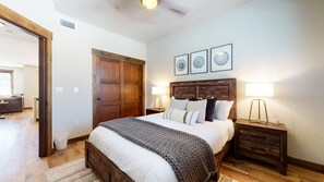 Une chambre à coucher avec un lit en bois, deux tables de chevet avec des lampes, une grande porte en bois et trois tableaux encadrés accrochés au mur.