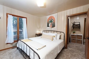 A bedroom with a bed, a nightstand, a window with curtains, a door, and a wall with a cactus painting. - Pet Friendly Cabin on 3.5 acres between Durango and Purgatory - Fire Pit (Durango)