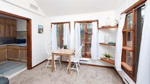 A cozy kitchen with wooden cabinets and a microwave, a dining area with a wooden table and white chairs, and a large window with curtains. - Pet Friendly Cabin on 3.5 acres between Durango and Purgatory - Fire Pit (Durango)
