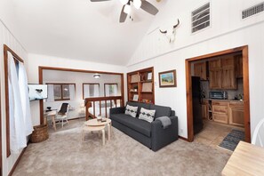 A cozy living room with a dark grey sofa, a small wooden coffee table, and a TV mounted on the wall. There is a kitchen area with wooden cabinets and a refrigerator. - Pet Friendly Cabin on 3.5 acres between Durango and Purgatory - Fire Pit (Durango)