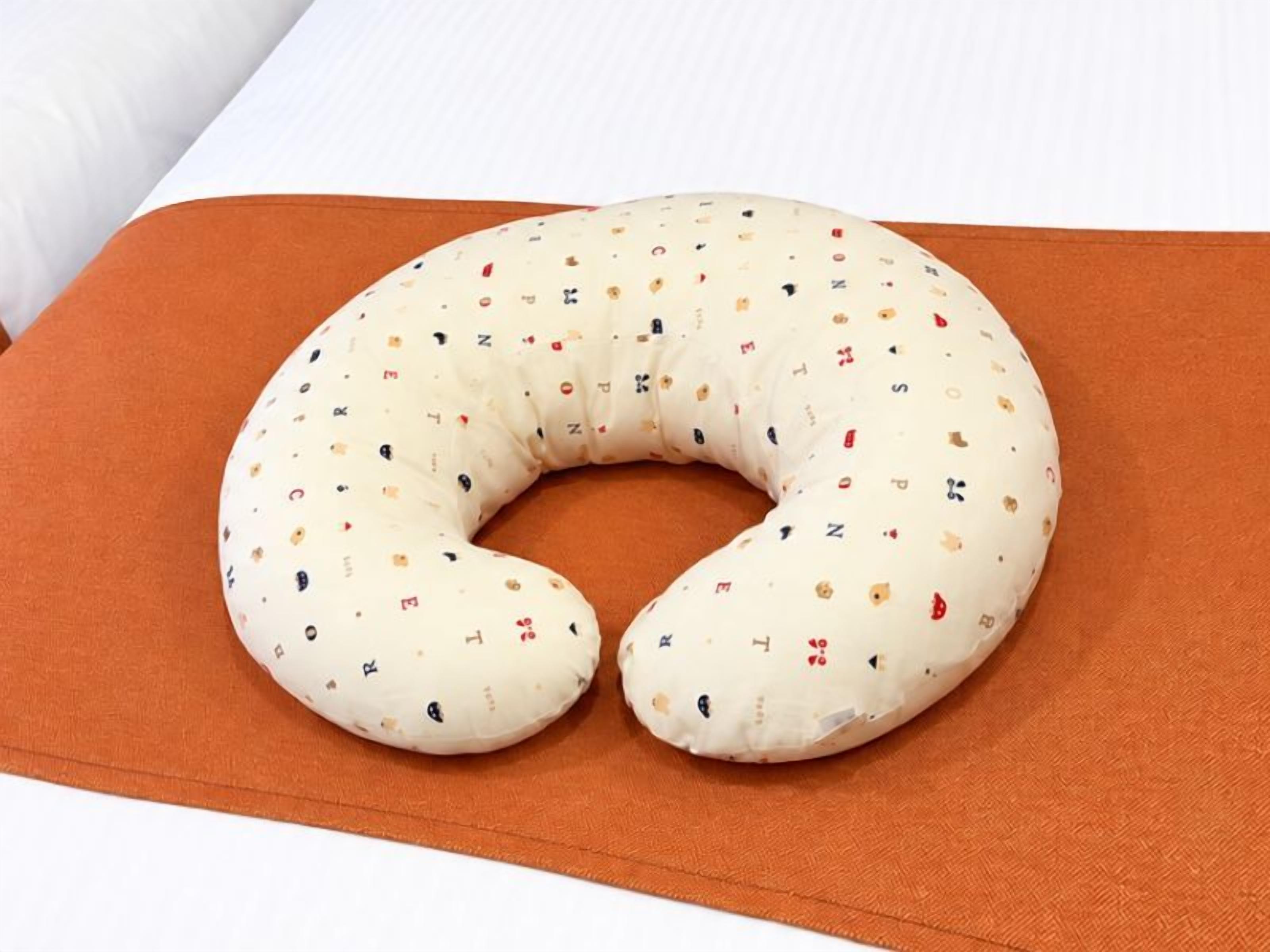 Ein weißes, halbmondförmiges Stoff-Babyschwungkissen mit bunten Buchstaben und Symbolen auf einem orangen Kissen.