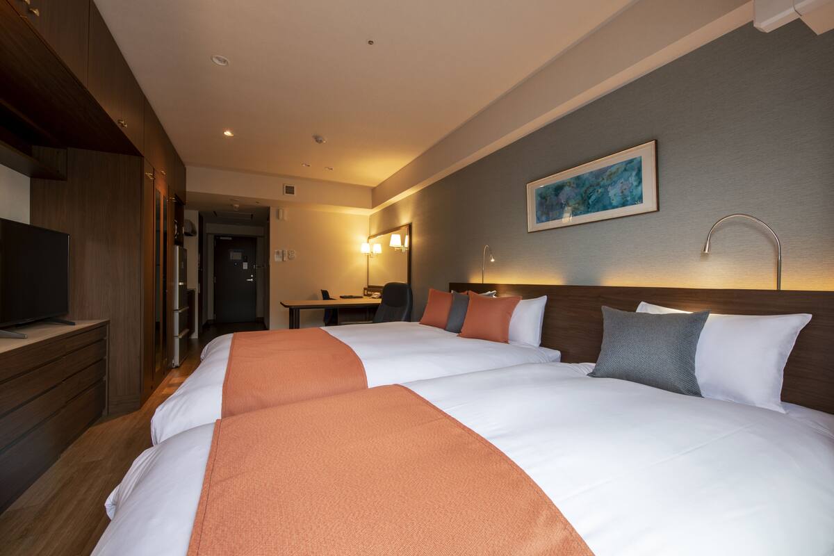 Una habitació d'hotel amb dos llits, un escriptori, una televisió i un quadre a la paret.